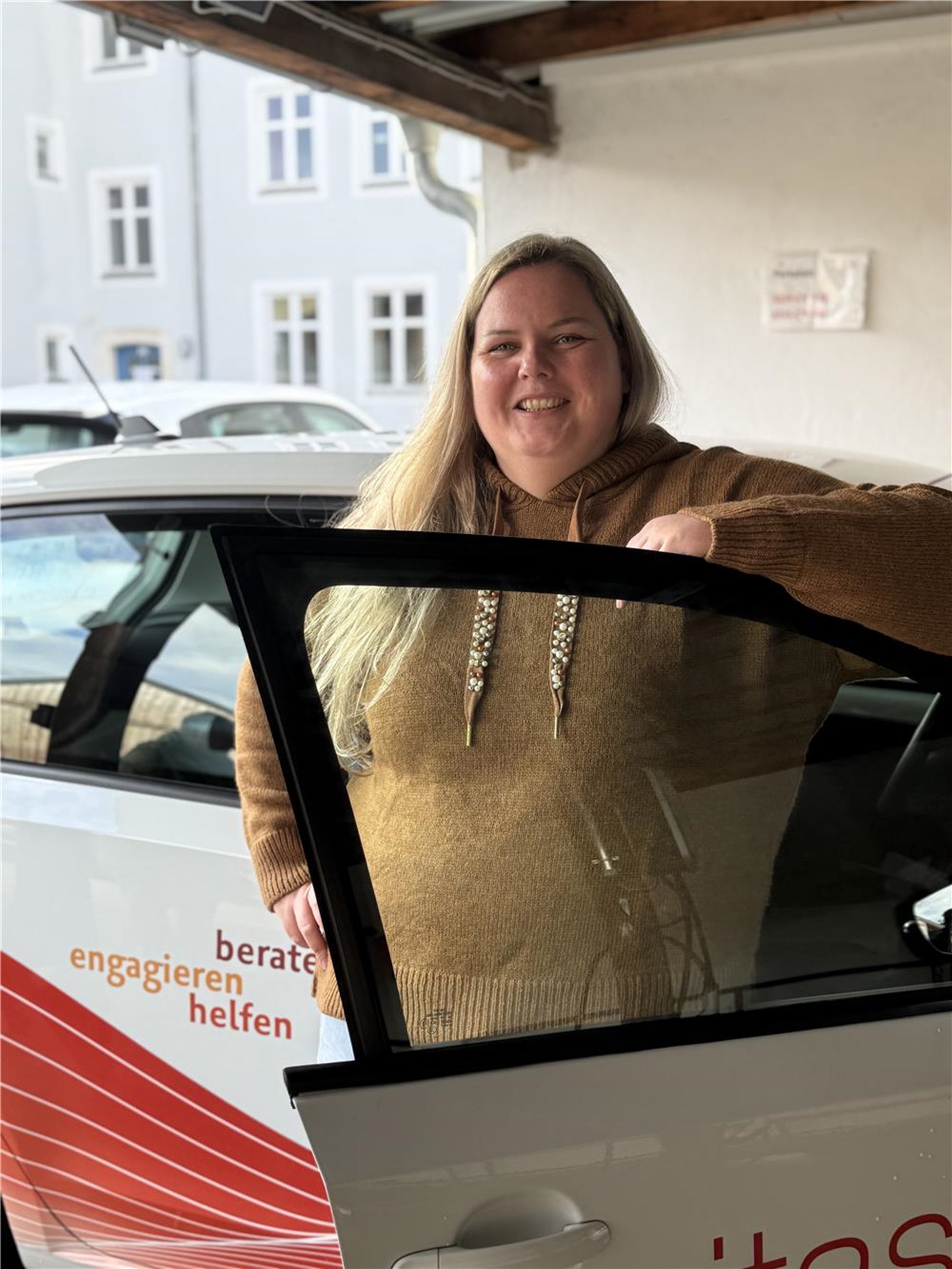 Eine Frau steht in einer geöffneten Fahrertür.