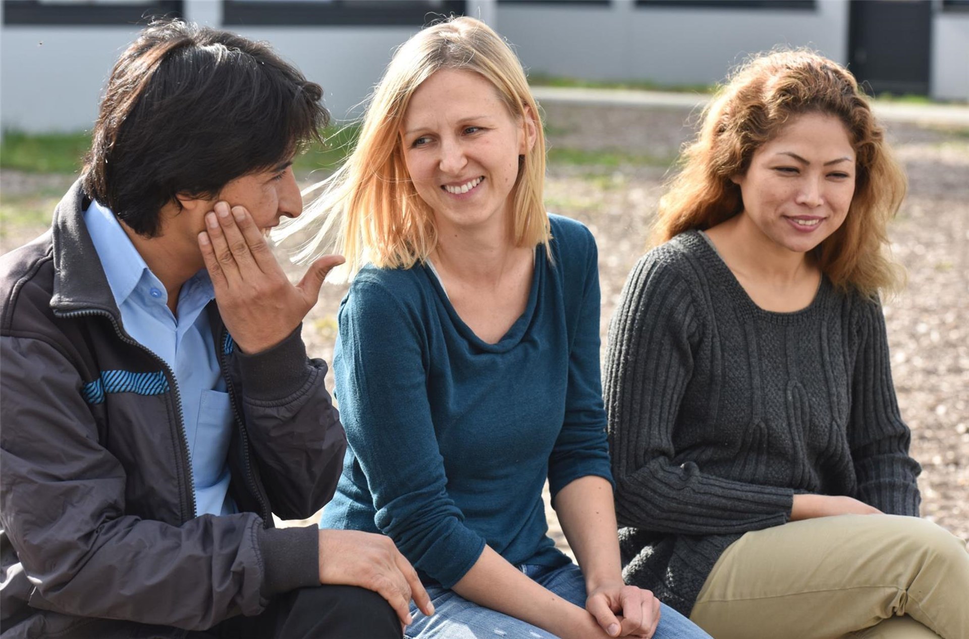 Drei junge Menschen unterschiedlicher Ethnie sitzen gemeinsam lachend zusammen